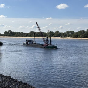Versorgungsschiff mit Kran auf der Weser bei Bremen-Farge, im Vordergrund die Steinschüttung am Ufer